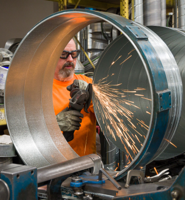 sparks fly as a worker uses a grinder on large metal cylinders