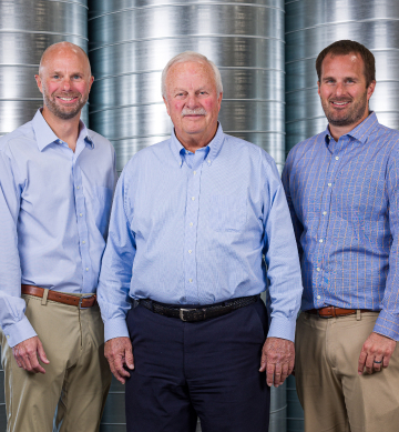 three engineers stand smiling in front of industrial equipment